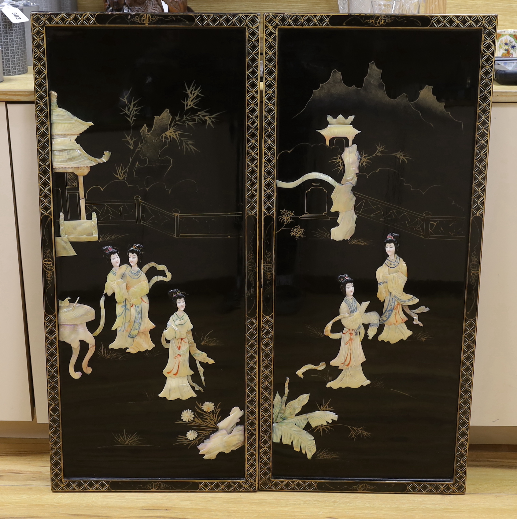 A pair of Chinese black lacquered panels, decorated in relief with females before pagodas, 92cm x 40cm